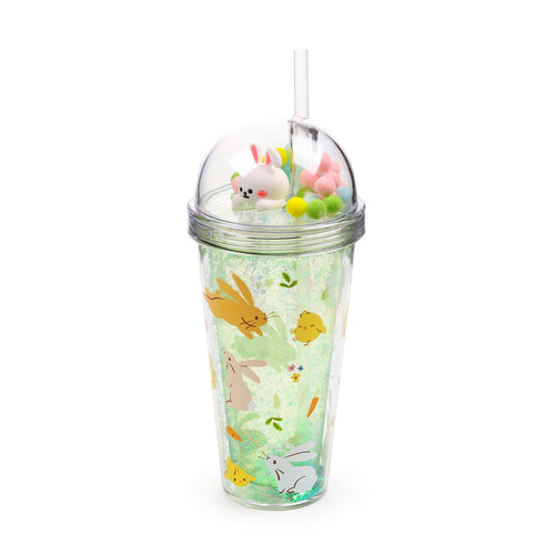 Clear double-walled plastic cup with light green glitter between its walls, decorated with springtime illustrations of bunnies, chicks, carrots, and flowers. It has a transparent domed lid enclosing a white bunny charm and colourful pink, yellow, and green pom-poms, complete with a clear drinking straw.