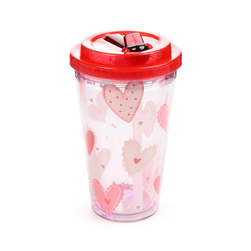 Angled view of a clear double-walled cup, decorated with pink and red heart patterns and iridescent heart glitter inside its walls. Topped with a bright red lid featuring a flip-top straw opening.