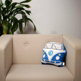 Lifestyle shot of a blue and white plush Volkswagen T1 Camper Bus shaped cushion, displaying its iconic front design and logo, on a cream armchair.