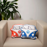 In-context lifestyle shot of a blue and white Volkswagen VW T1 Camper Bus plush shaped cushion, alongside a red and white matching cushion, resting on a beige armchair.