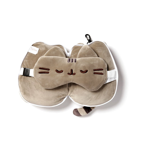 Overhead view of a light brown Pusheen cat-shaped travel pillow and eye mask set. The soft pillow has ear shapes and a striped tail, with the matching eye mask, featuring embroidered closed eyes and whiskers, placed on top. A white zipper, black carabiner clip, and white adjustable strap are also visible.