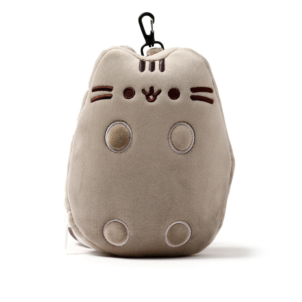 Front view of a beige plush cat-shaped travel pillow and eye mask set, featuring embroidered circular eyes, a pink nose, mouth, whiskers, three forehead stripes, and four circular belly markings, with a black carabiner clip attached at the top.