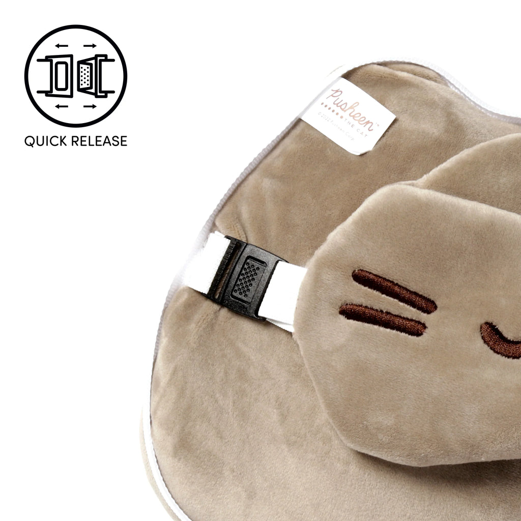 Angled close-up of a beige plush travel pillow, featuring a black quick-release buckle on a white strap. A matching beige plush eye mask with dark brown embroidered cat whiskers rests on the pillow. A white product label is also partially visible.