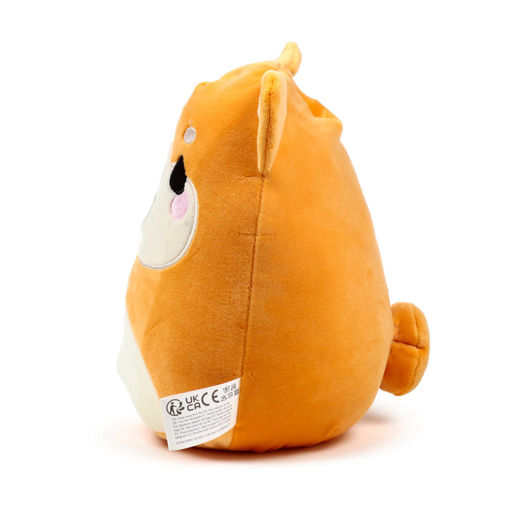 Left side view of a round orange and white Shiba Inu dog plush toy, showing black embroidered eye and nose, pink cheek marks, a curled tail, and a white fabric warning label.