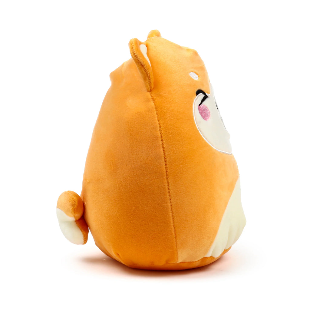 Angled view of an orange and cream-coloured Squidglys Shuggs Shiba Inu dog plush toy, featuring one pointed ear, a small tail, and an embroidered eye with a pink blush.