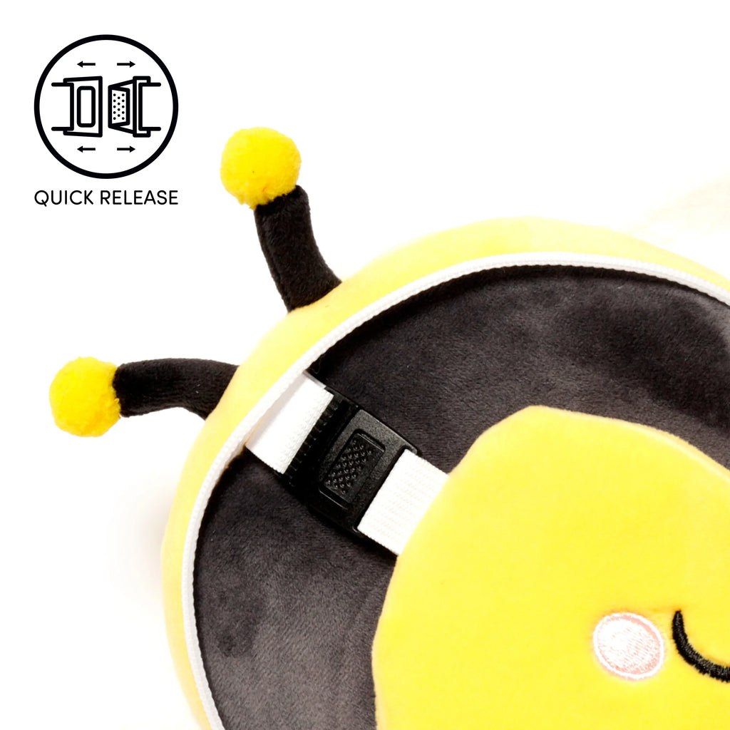 Close-up angled view of a plush yellow and black bee travel pillow. It features black antennae with yellow tips, a white adjustable strap with a black quick-release buckle, and part of an embroidered winking eye.