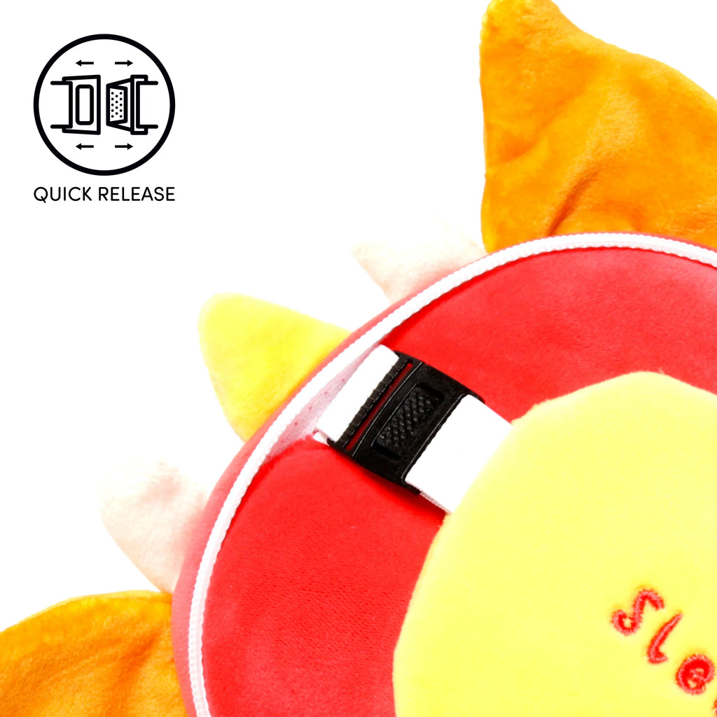 Close-up detail of a travel pillow, showing a black quick-release buckle on a white strap, nestled within its plush red, yellow, and orange fabric. Partial red embroidered text 'Sle...' is visible on the yellow section. A 'QUICK RELEASE' graphic icon is displayed in the top left.