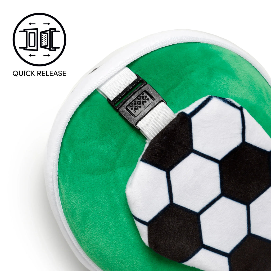 Close-up of a green travel pillow, partially revealing a football-patterned eye mask with black and white hexagons. A white strap with a black quick-release buckle is visible against the green pillow.