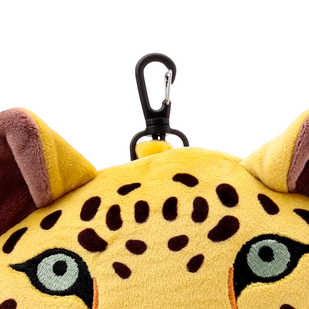 Close-up of a soft yellow leopard print travel pillow featuring embroidered light blue-grey eyes and brown ears, with a black carabiner clip at the top.