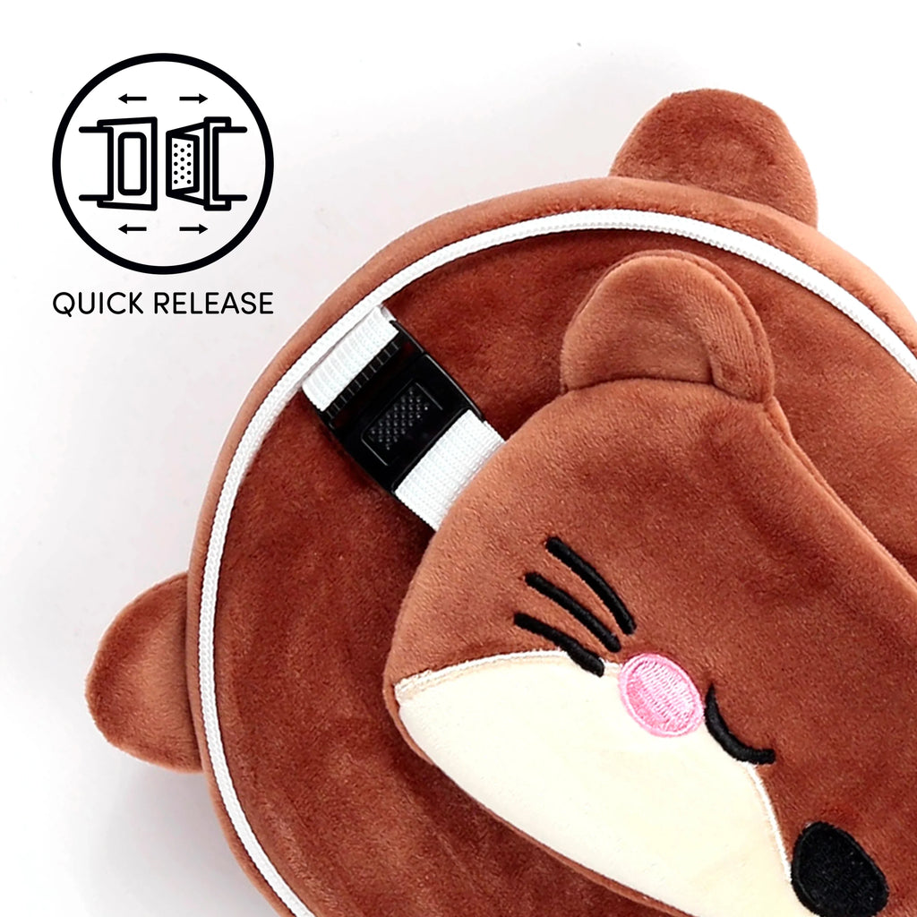 Close-up, angled view of a brown plush otter travel pillow and matching eye mask. The pillow features white piping and a white quick-release buckle. The eye mask has an embroidered otter face with pink cheeks and black whiskers.