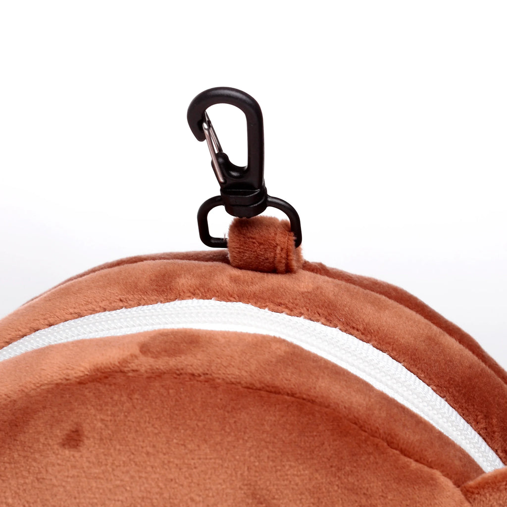 Close-up of a brown plush travel pillow, showing a white zip and a black carabiner clip attached to a fabric loop.