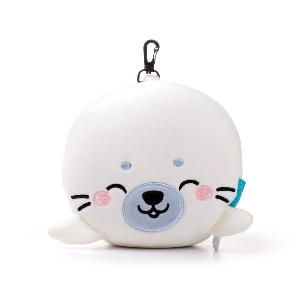 Front view of a white plush seal-shaped travel pillow, with embroidered blue eyes, pink cheeks, and a light blue muzzle. A black carabiner clip is attached at the top.