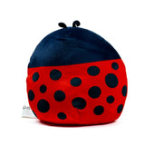 Angled view of a Tilly the Ladybug plush toy, depicting a rounded red body with black spots, a dark blue head, and small black antennae.
