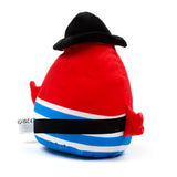 Red plush toy, seen from behind, wearing a black hat. It has blue, white, and black horizontal stripes around its base and small red fin-like appendages on its sides. A white safety tag is visible on the lower left.