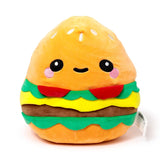 Front view of a plush burger toy with an orange bun, green lettuce, red tomatoes, yellow cheese, and a brown patty. It has an embroidered cute face with black eyes, a smile, pink cheeks, and white sesame seeds on the bun.