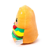 Angled view of a soft plush burger toy, showing its orange bun with embroidered sesame seeds, green lettuce, yellow cheese, brown patty, and red tomato layers, alongside a cute embroidered face with black eyes and pink cheeks.