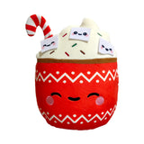 Front view of a hot chocolate plush toy. It has a red base with white zigzag patterns and an embroidered smiling face, topped with cream-coloured plush, colourful sprinkles, three small smiling white felt characters, and a red and white striped candy cane.