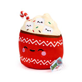 Angled view of a hot chocolate plush toy with a red cup base featuring white zig-zag patterns and dots, and an embroidered face with closed eyes and pink cheeks. The cream-coloured top includes three happy-faced marshmallow plush pieces, colourful sprinkles, and a red and white striped candy cane.