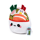 Angled view of a cute Squidglys Foodiemals ramen bowl plush toy. The soft white plush features an embroidered smiling face with pink cheeks. The top is decorated with yellow noodles, a narutomaki swirl, green seaweed pieces, red felt pieces, and a cartoon egg character with a face. A hang tag is visible on the side.