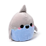 Angled view of a soft grey and light blue plush shark toy, with a dorsal fin, embroidered black eyes, a smiling mouth, pink cheek blush, and grey gill details.