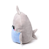 Angled view of a soft, grey and light blue plush shark toy, showing its black eyes, pink cheeks, stitched gills, and fins, on a white background.