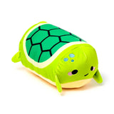 Angled view of a squishy green Squidglys Altas the Turtle plush toy, showing its lighter green body, darker green patterned shell, and embroidered facial features.