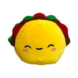 Front view of a Squidglys Foodiemals Frida the Taco plush toy, a cheerful yellow taco with green, red, and brown fillings, an embroidered smiling face, and pink blush.