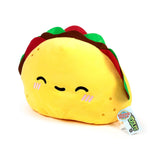 Angled view of a yellow plush taco toy with a happy embroidered face and pink blush, showing red, green, and brown fillings.