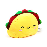 Angled view of a yellow taco plush toy with red, brown, and green fillings, featuring a smiling embroidered face with pink blush.