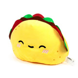 Angled view of a yellow taco plush toy with brown, red, and green fillings, featuring a smiling embroidered face and small golden embroidered details.