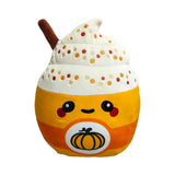 Front view of the 'Hazel the Spiced Latte' Squidglys plush toy. It's a yellow and orange cup shape with a cute embroidered face, a pumpkin logo, white whipped cream with colourful sprinkles, and a brown cinnamon stick.