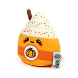 Angled view of a Squidglys 'Hazel the Spiced Latte' plush toy. This cute orange and cream soft toy is shaped like a drink with whipped cream, an embroidered face, a pumpkin design on its front, decorative sprinkles, and a brown cinnamon stick. Product tags are visible on the side.