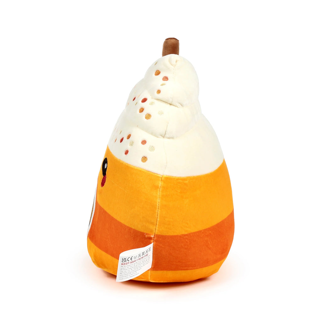 Angled view of a spiced latte plush toy, featuring a cream-coloured whipped topping with embroidered orange sprinkles and a brown stick. Its body is orange with a dark orange stripe, and a white fabric care label hangs from its side.