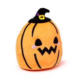 Angled view of an orange plush pumpkin toy wearing a black witch's hat with a purple band and yellow buckle. It features black triangular eyes, a jagged black mouth, and pink circular blush marks.
