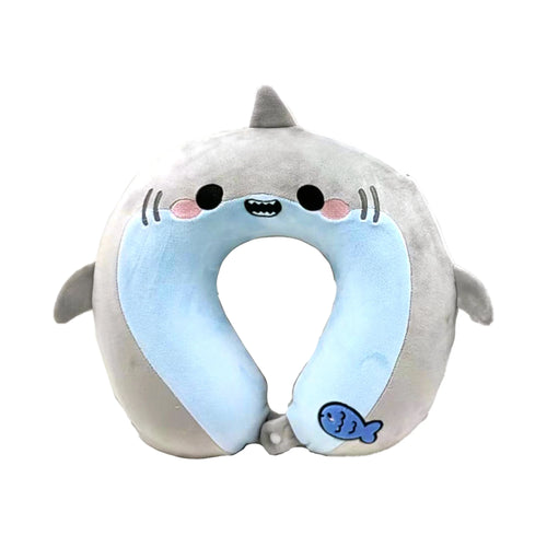 Front view of a plush, grey and light blue shark-shaped memory foam travel pillow, featuring cartoon eyes, a grinning mouth with teeth, pink cheeks, gills, a fin on top, and a small blue fish graphic.
