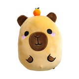Front view of a light brown Squidglys Duke the Capybara plush toy, featuring embroidered black eyes, pink cheeks, a dark brown nose and mouth, and dark brown ears. A small orange fruit with a green stem is perched on its head.