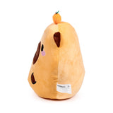 Angled view of a light brown Capybara plush toy with dark brown ears, an embroidered eye, nostril, and pink cheek on one side, and a small orange fruit with a green stem on its head. A white product label is visible on its lower back seam.