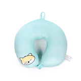 Top-down view of a light blue plush travel pillow, featuring a sleeping Shiba Inu character face. It includes a hanging loop, a snap fastener, and a fabric care tag.