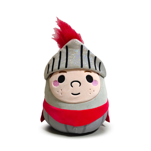Front view of a Squidglys Knights & Dragons knight plush toy, featuring a pale-faced character with black eyes, a small nose, smiling mouth, pink blush, and small brown freckles. The soft toy wears a shimmering grey helmet with black details and a bright red feathery plume, complemented by a red sash over its grey body.