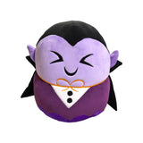 Front view of a purple Dracula plush toy with embroidered V-shaped eyes, a smile, and pointed ears, wearing a black and purple tuxedo-style outfit with an orange bow tie, on a white background.