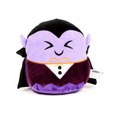 Front view of a round, lavender and dark purple Spooky Dracula plush toy with a happy embroidered face, pointed ears, black cape, white shirt front with an orange bow tie, and dark purple waistcoat, against a white background.