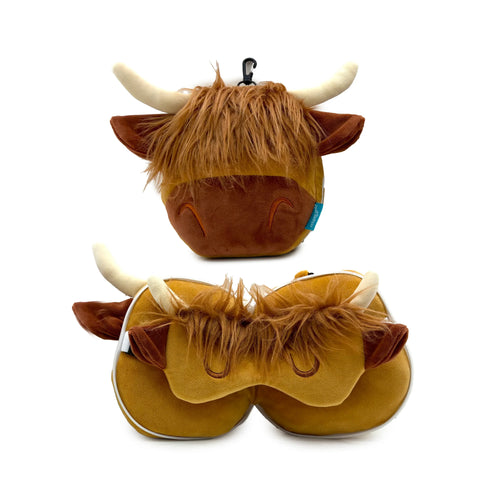 Front view of a fluffy, brown Highland coo travel pillow with light horns, shaggy fur, and embroidered sleepy eyes. Below it, a matching Highland coo eye mask, also with shaggy fur, light horns, and embroidered sleepy eyes, shows a white zip along its edge.