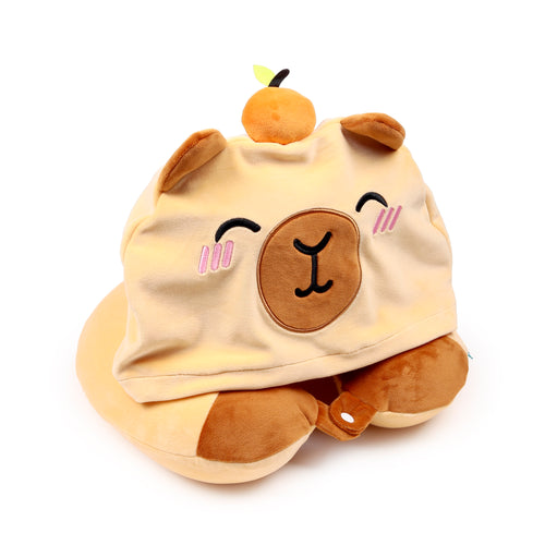 Angled view of a plush capybara travel pillow and hood. The pale brown pillow features a cute capybara face with closed eyes and pink blush, topped with a small orange fruit and green leaf.
