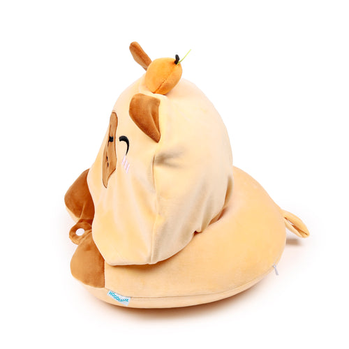 Angled rear view of a soft, light brown Hoodeazzz capybara travel pillow and hood. The plush hood features brown ears, partially visible embroidered facial details, and an orange accent with a green stem on top, all sitting on a U-shaped pillow base.