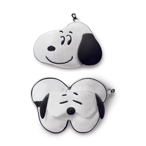 Overhead view of a white and black Peanuts Snoopy travel pillow and eye mask set. The image shows the pillow in its compact Snoopy head form with a carabiner clip, and unfurled, revealing the integrated eye mask with embroidered closed eyes.