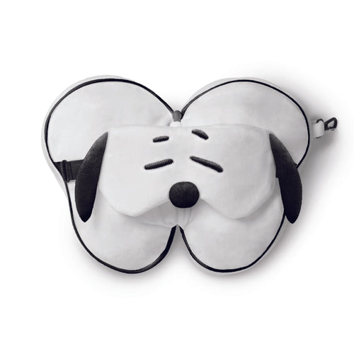 Angled overhead view of a white Snoopy travel pillow and eye mask set. The eye mask features black closed eyes, a nose, and floppy ears, on top of the folded white pillow with black piping and a zip. An adjustable black strap and clip are visible.