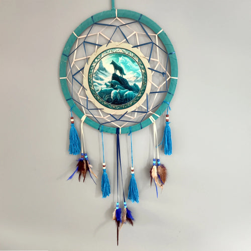 Front view of a teal dreamcatcher with a central wolf pack illustration against a mountain backdrop. It features blue tassels, multicoloured beads, and brown and blue feathers.