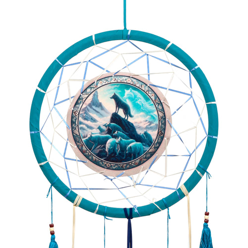 Front view of a teal dreamcatcher with an intricate white and light blue web, featuring a central circular design of a wolf pack in a snowy mountain landscape, including an ethereal spirit wolf. Dark blue tassels with brown and cream beads hang from the bottom.