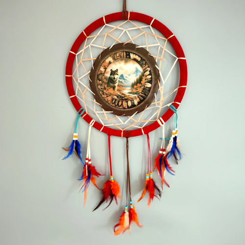 Front view of a red dreamcatcher featuring a central autumnal wolf design, with decorative orange, blue, and brown feathers and beads hanging below.
