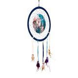 Front view of a dark blue dreamcatcher featuring a central illustration depicting a white unicorn and a small fairy in a mystical blue and green forest. It is adorned with colourful ribbons, wooden beads, and mixed feathers.